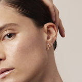 Close-up of a woman wearing a gold earring with a beige background