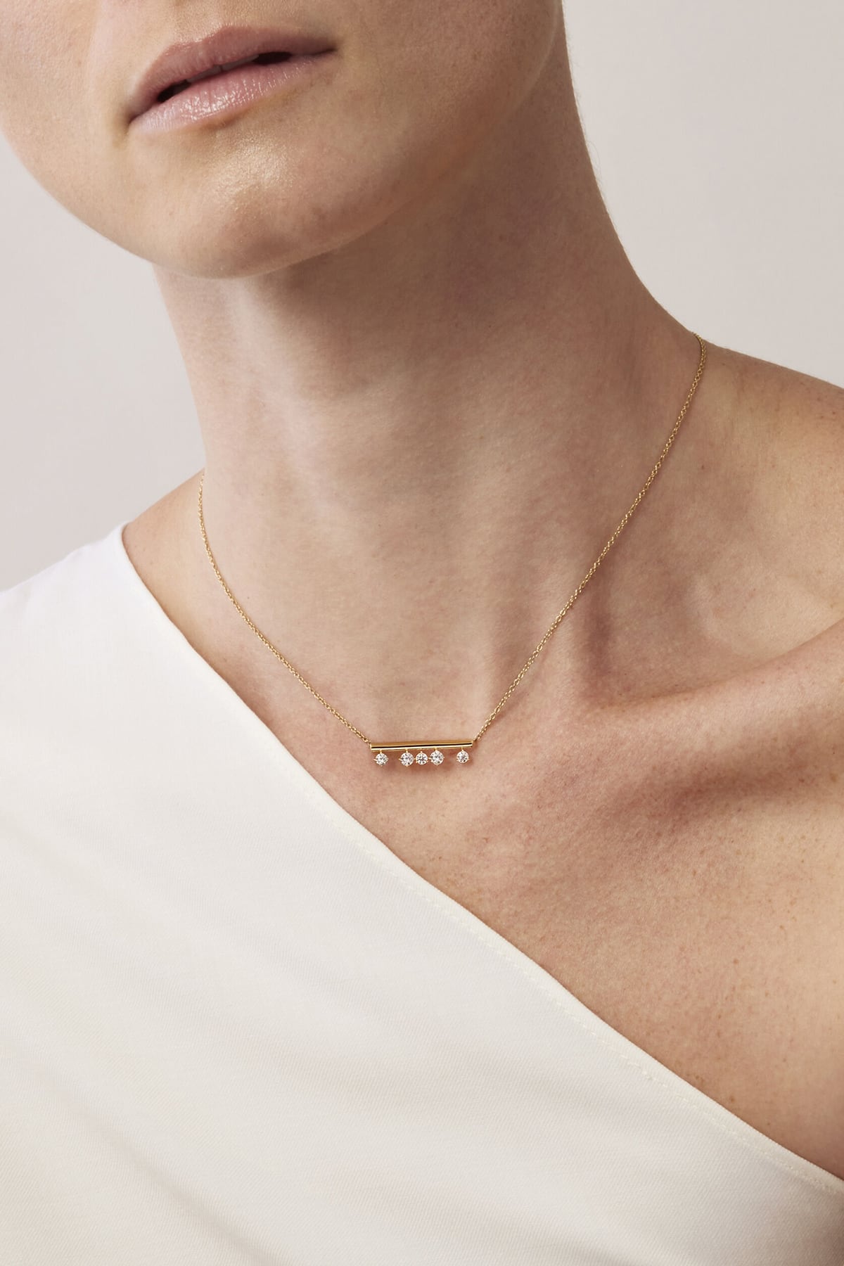 Necklace with small beads on a person wearing a white top against a neutral background