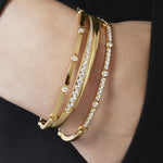 Gold bracelets with clear stones on a wrist against a black background