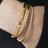 Gold bracelets with clear stones on a wrist against a black background