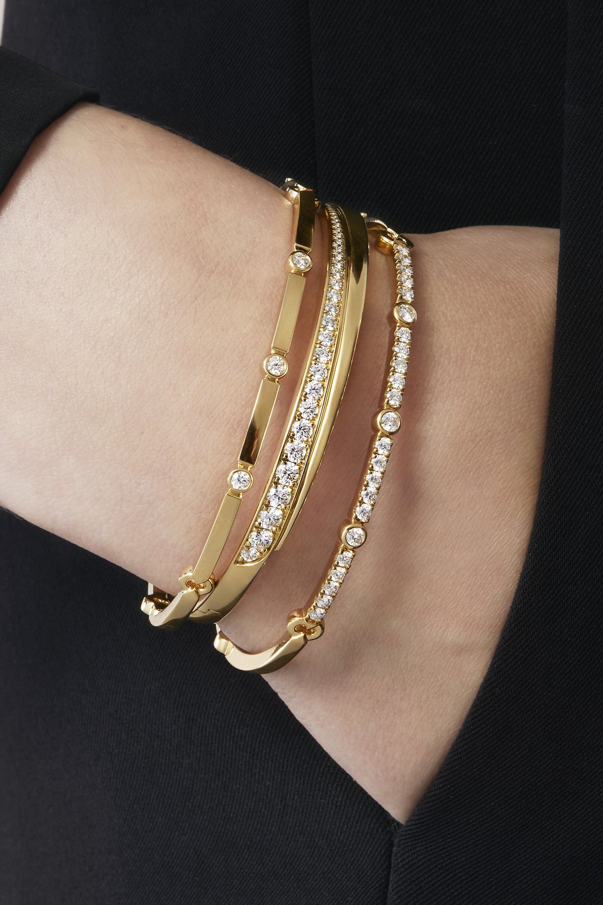 Gold bracelets with clear stones on a wrist against a black background