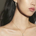 Woman wearing a gold necklace and earring against a neutral background