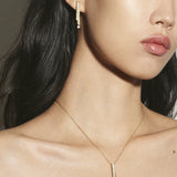 Woman wearing a gold necklace and earring against a neutral background