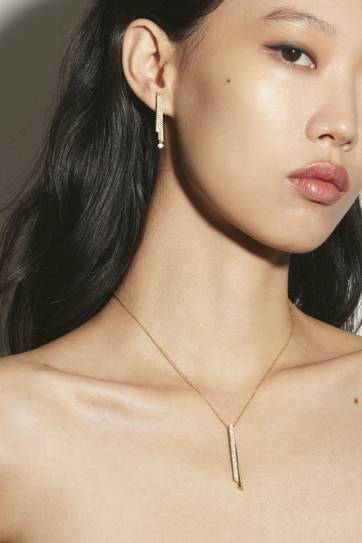 Woman wearing a gold necklace and earring against a neutral background