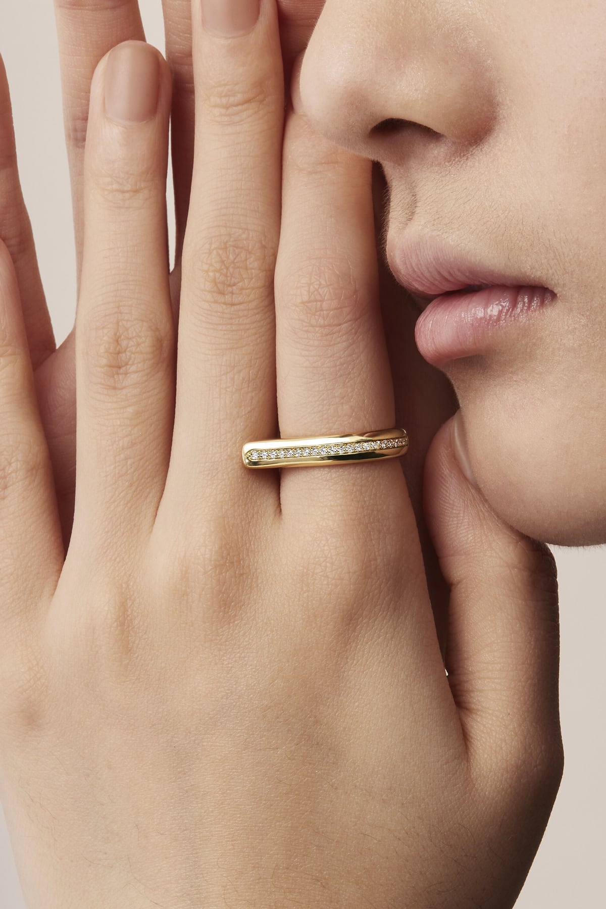Close-up of a hand wearing a gold ring with a beige background