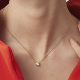 Gold necklace with a diamond pendant worn by a person in a red outfit.