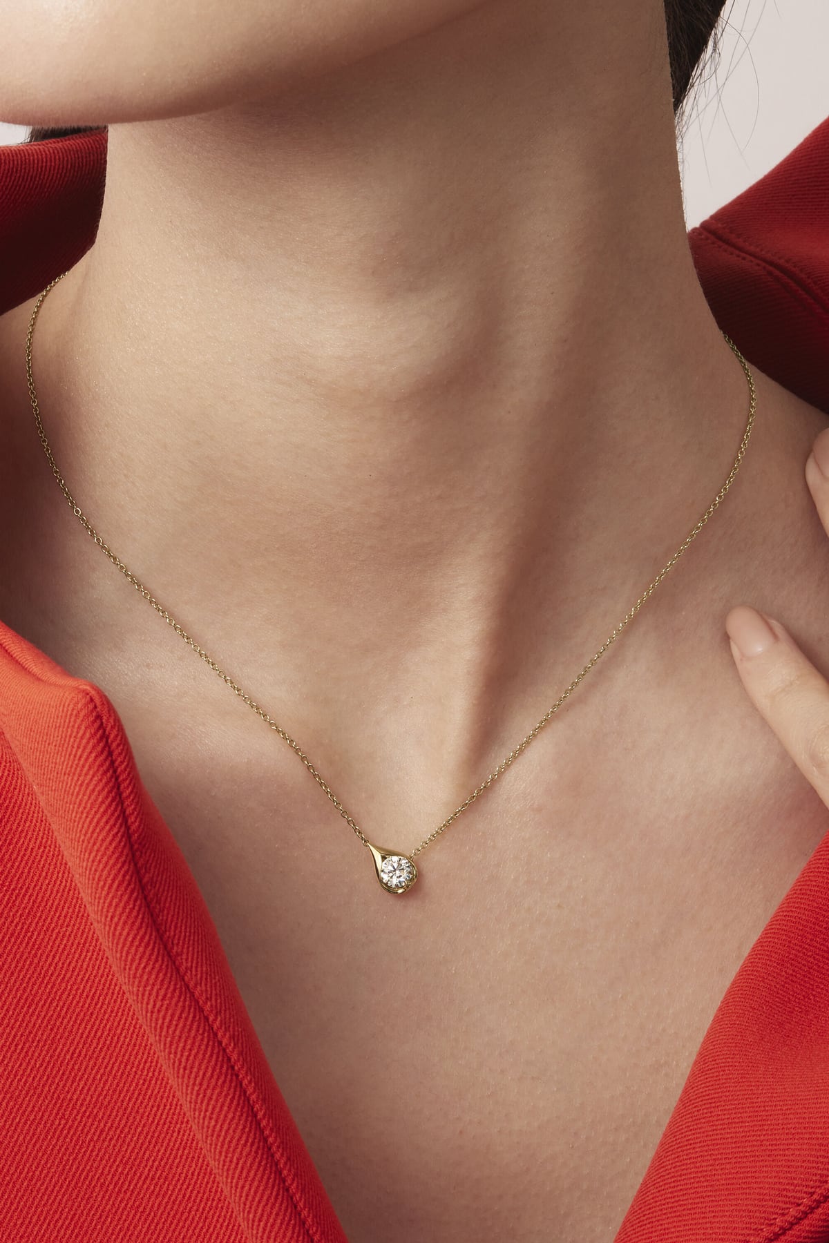 Gold necklace with a diamond pendant worn by a person in a red outfit.