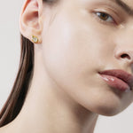 Close-up of a woman wearing a gold earring with a diamond on a neutral background