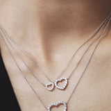 Two heart-shaped silver necklaces on a person's neck