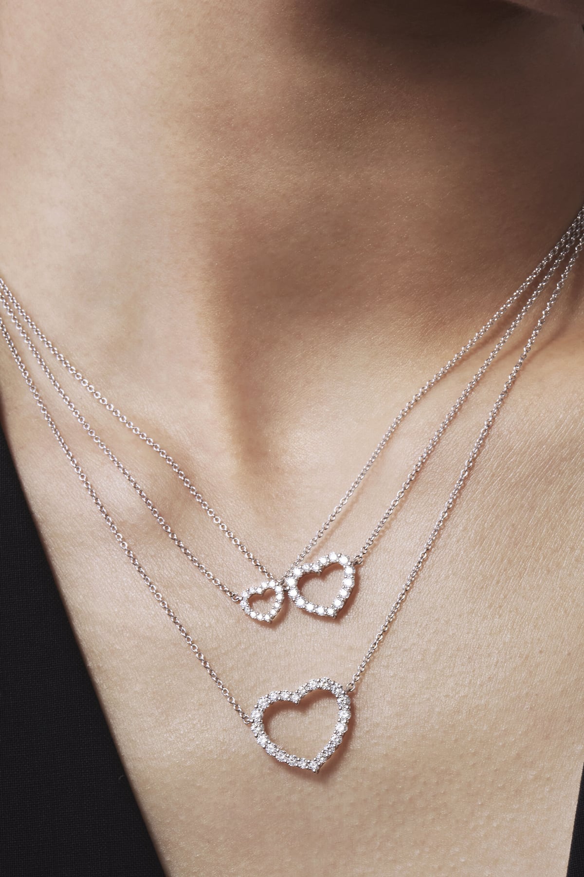 Two heart-shaped silver necklaces on a person's neck
