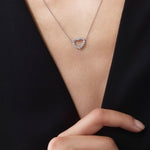 Heart-shaped necklace worn by a person with a hand pointing to it against a black background