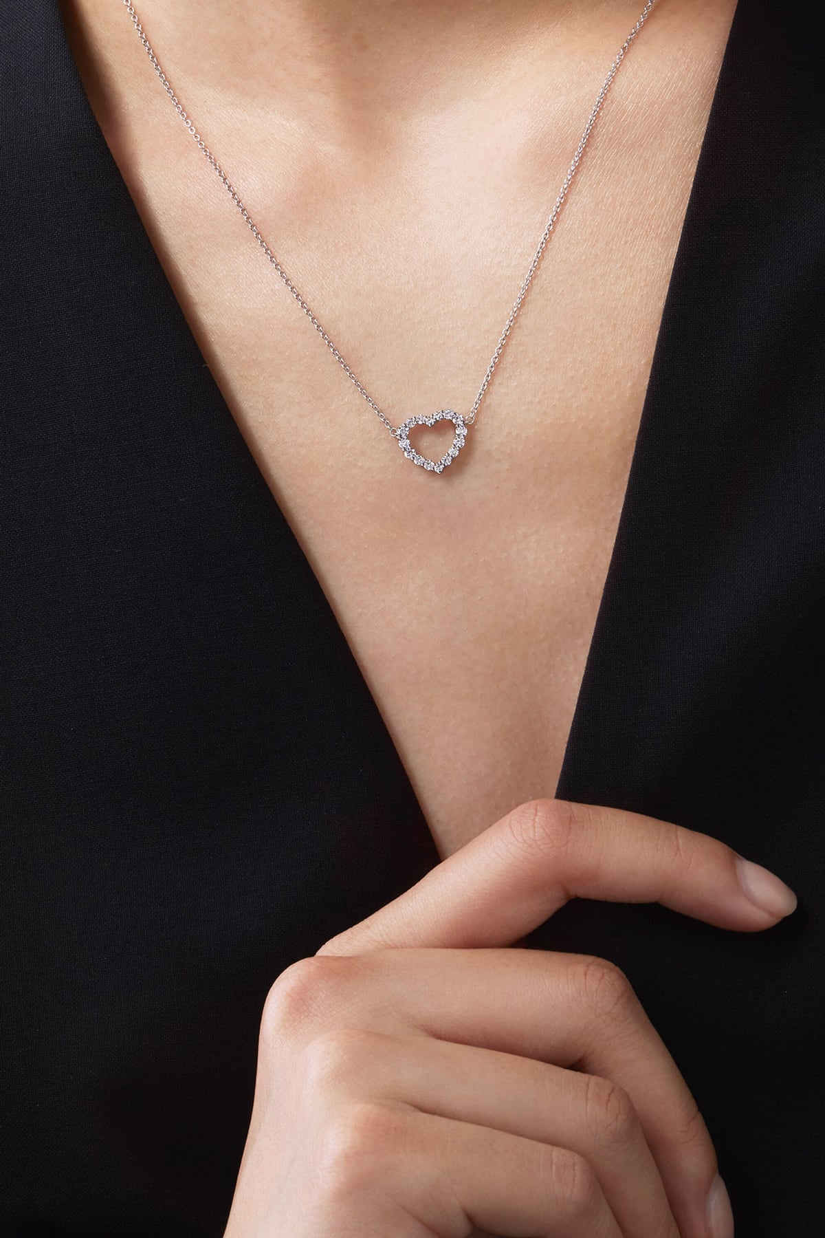 Heart-shaped necklace worn by a person with a hand pointing to it against a black background