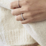 Close-up of a hand wearing two silver rings on a white sweater background