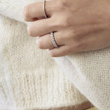 Close-up of a hand wearing two silver rings on a white sweater background