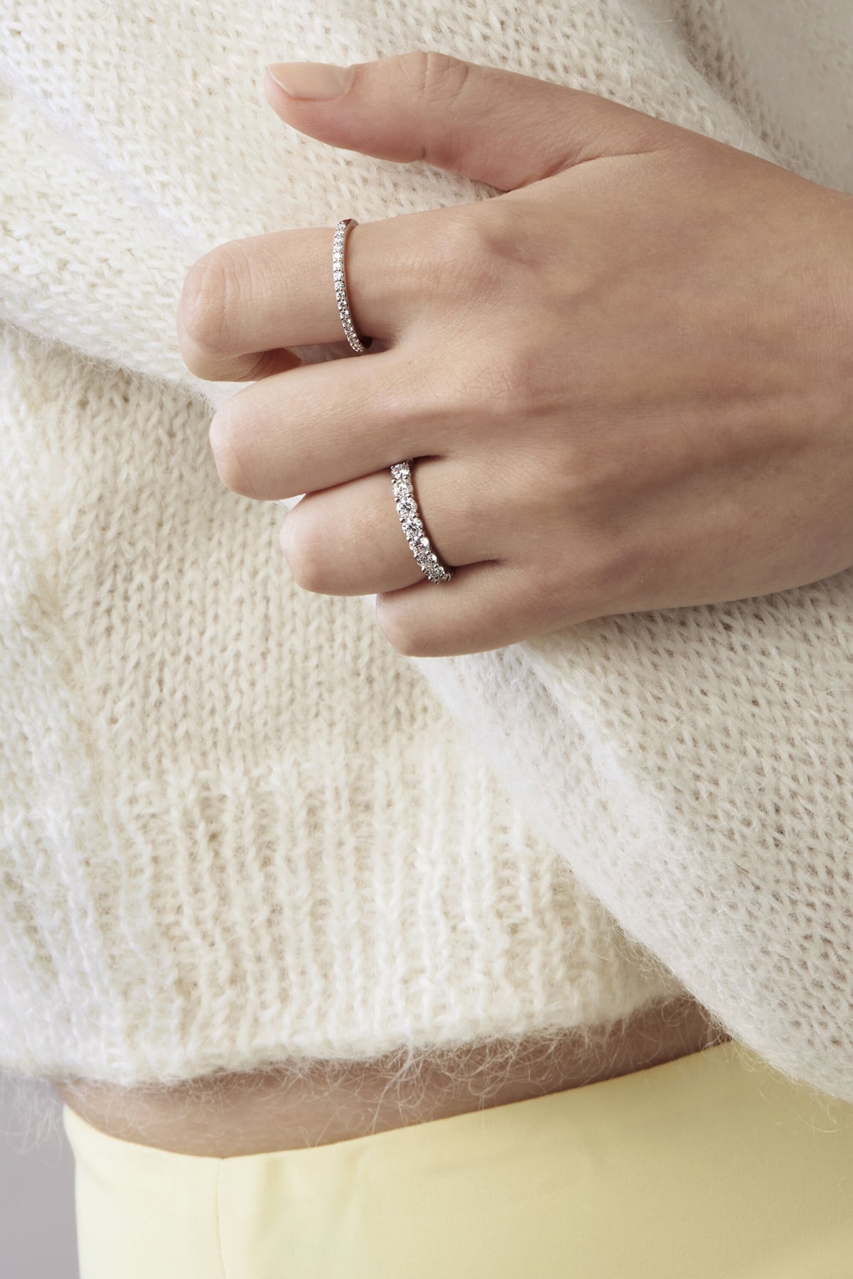 Close-up of a hand wearing two silver rings on a white sweater background