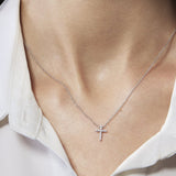 Necklace with a small cross pendant worn by a person wearing a white shirt.