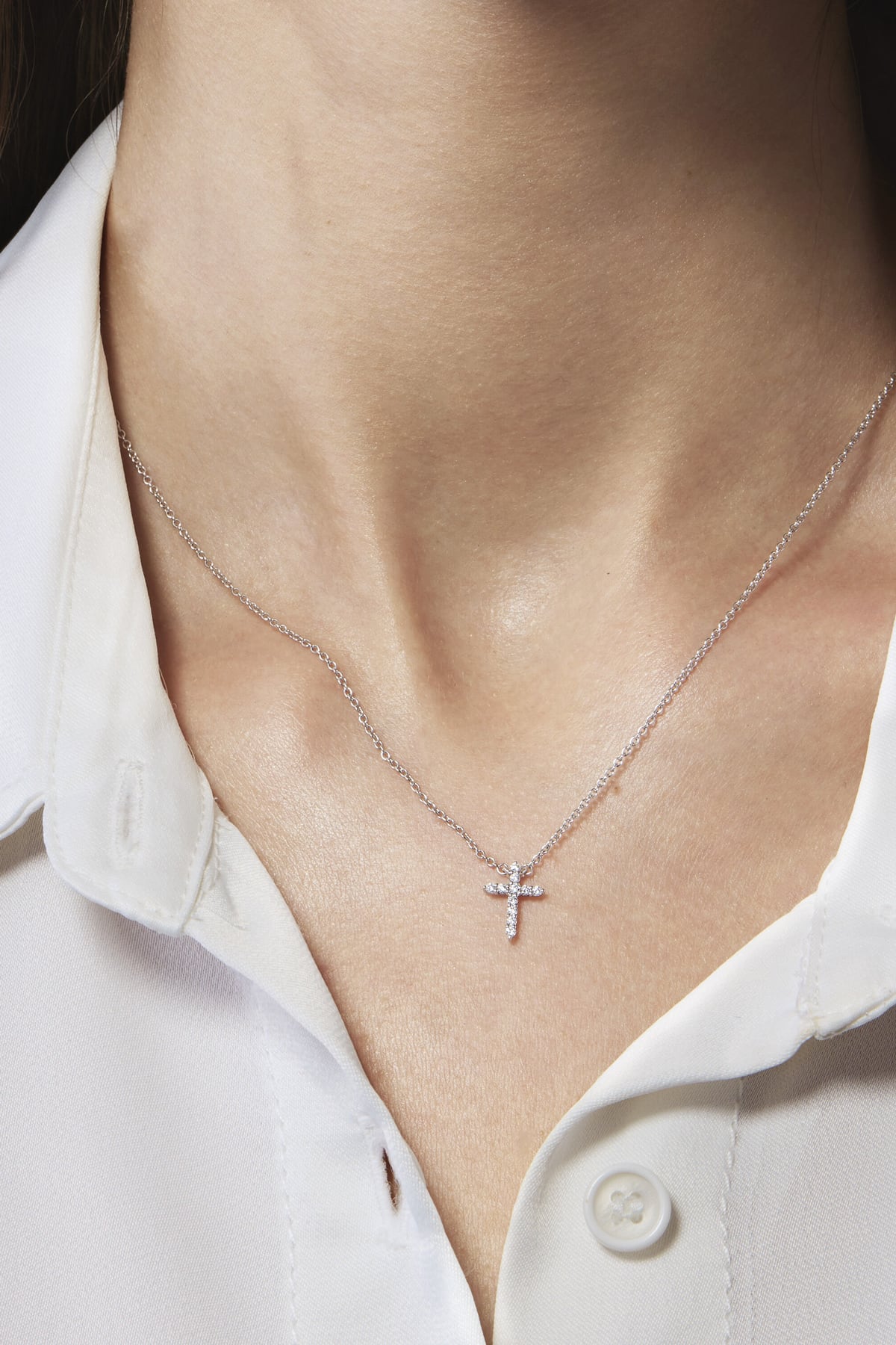 Necklace with a small cross pendant worn by a person wearing a white shirt.