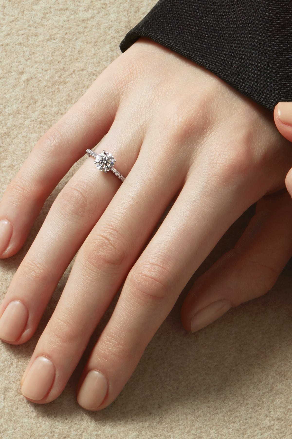 Close-up of a hand wearing a Hearts On Fire diamond ring on a beige background