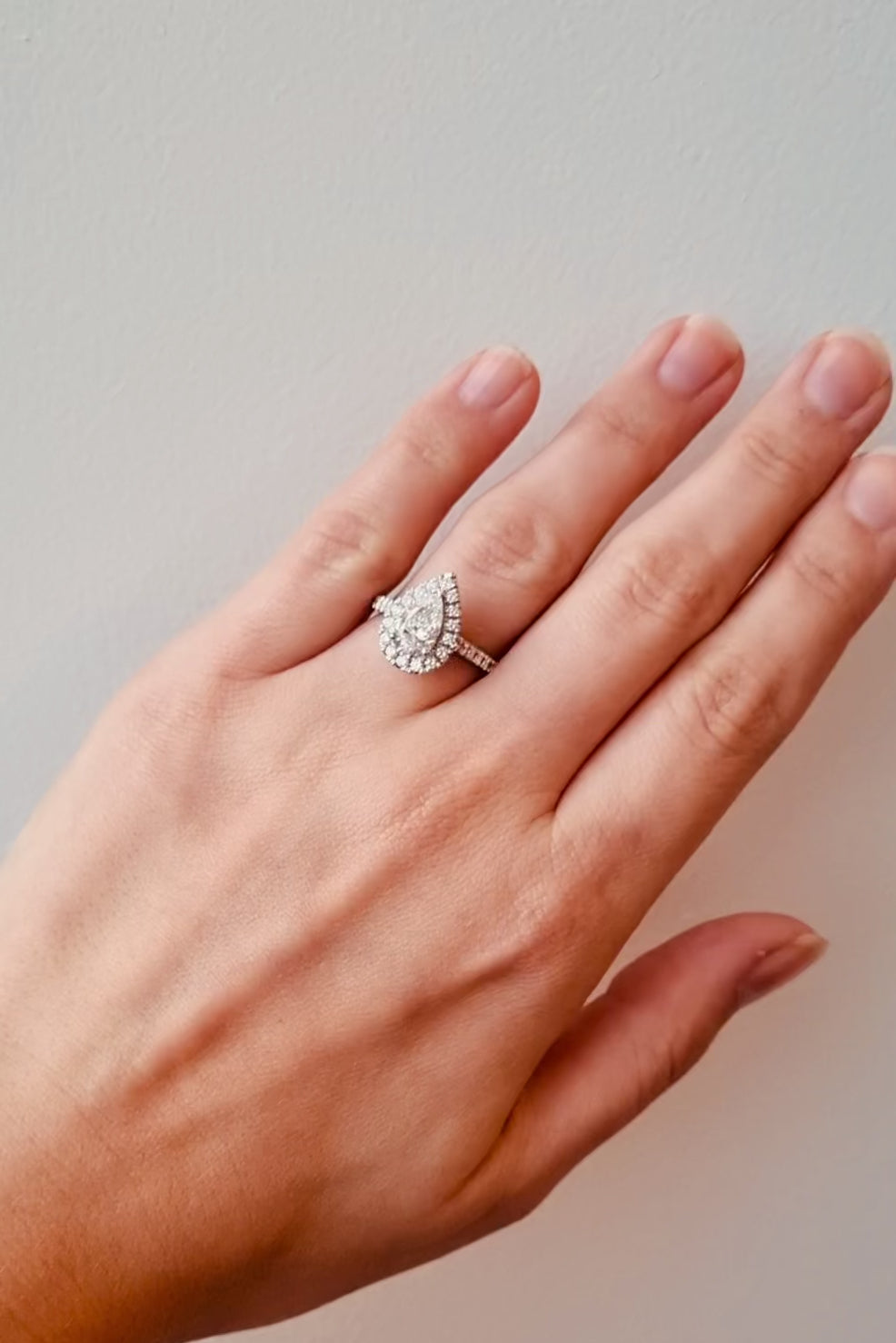 Diamond ring with a pear-shaped centre stone and diamond halo on a lady's hand