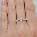 Hand wearing a silver ring with a diamond on a light grey background at LeGassick.
