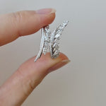 A close-up of a hand holding a delicate white gold ring set with small clear diamonds, photographed against a warm beige background with soft diagonal shadows.