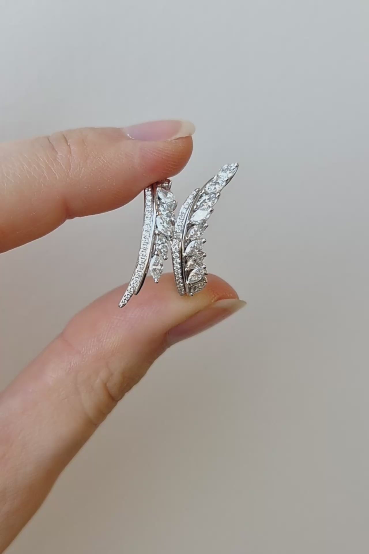 A close-up of a hand holding a delicate white gold ring set with small clear diamonds, photographed against a warm beige background with soft diagonal shadows.
