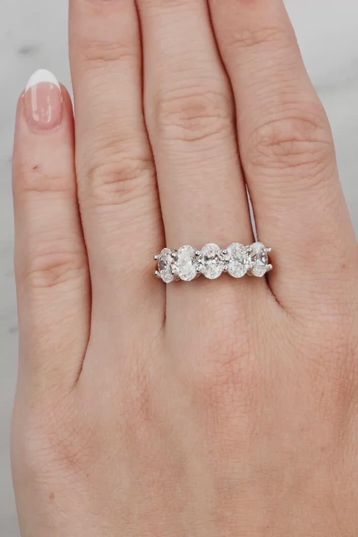 Silver ring with five diamonds on a hand with light pink nail polish against a light grey background at LeGassick.