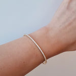 Gold diamond Bangle on a wrist against a light background