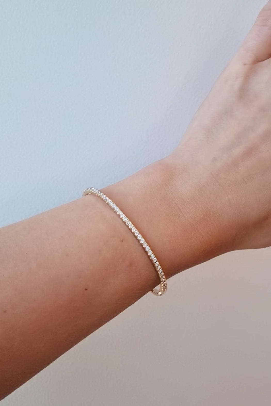 Gold diamond Bangle on a wrist against a light background