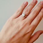 Hand wearing a gold ring with a diamond on a neutral background at LeGassick.