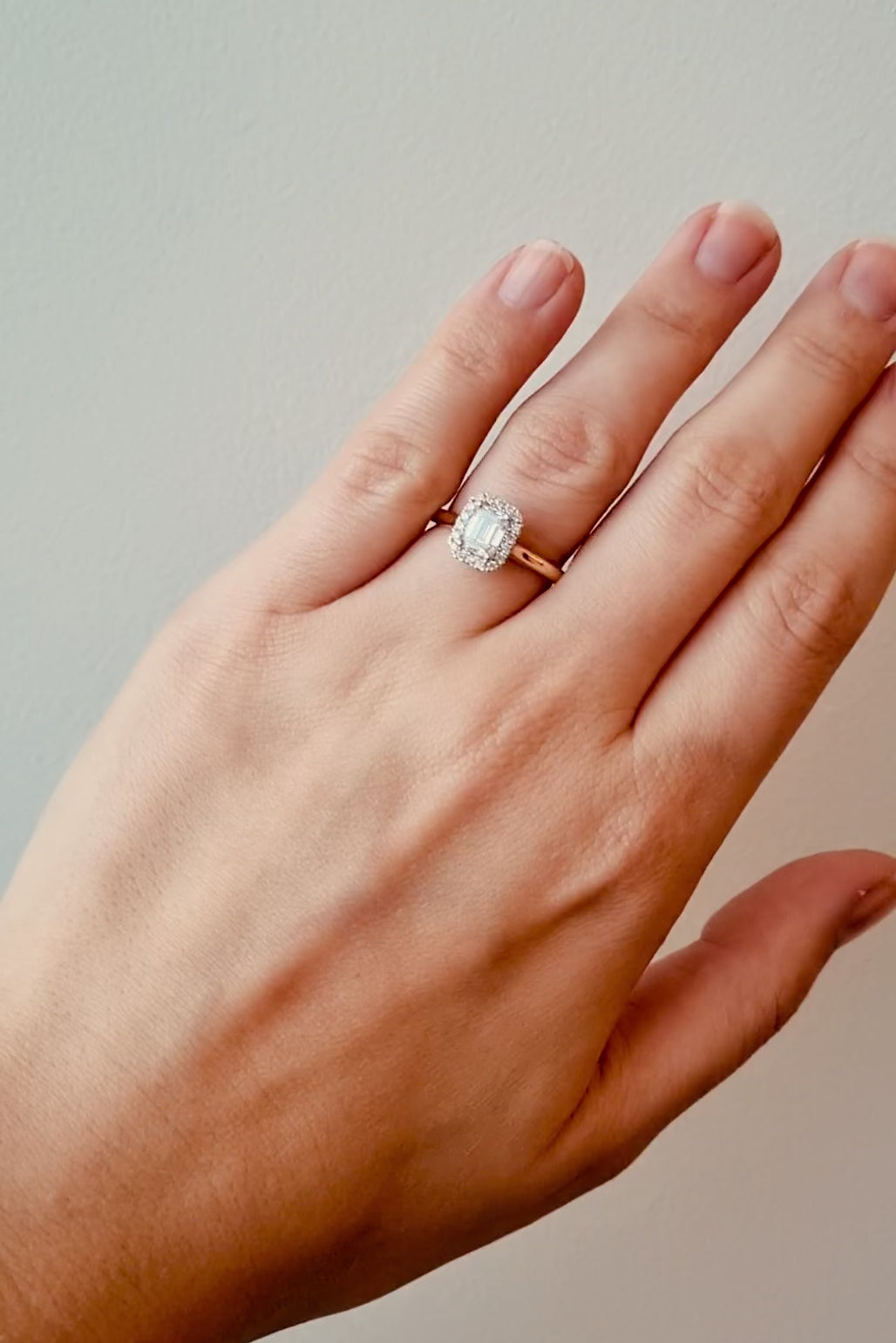 Hand wearing a gold ring with a diamond on a neutral background at LeGassick.