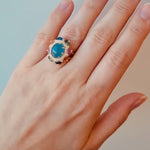 Ring with a blue gemstone on a hand against a brown background