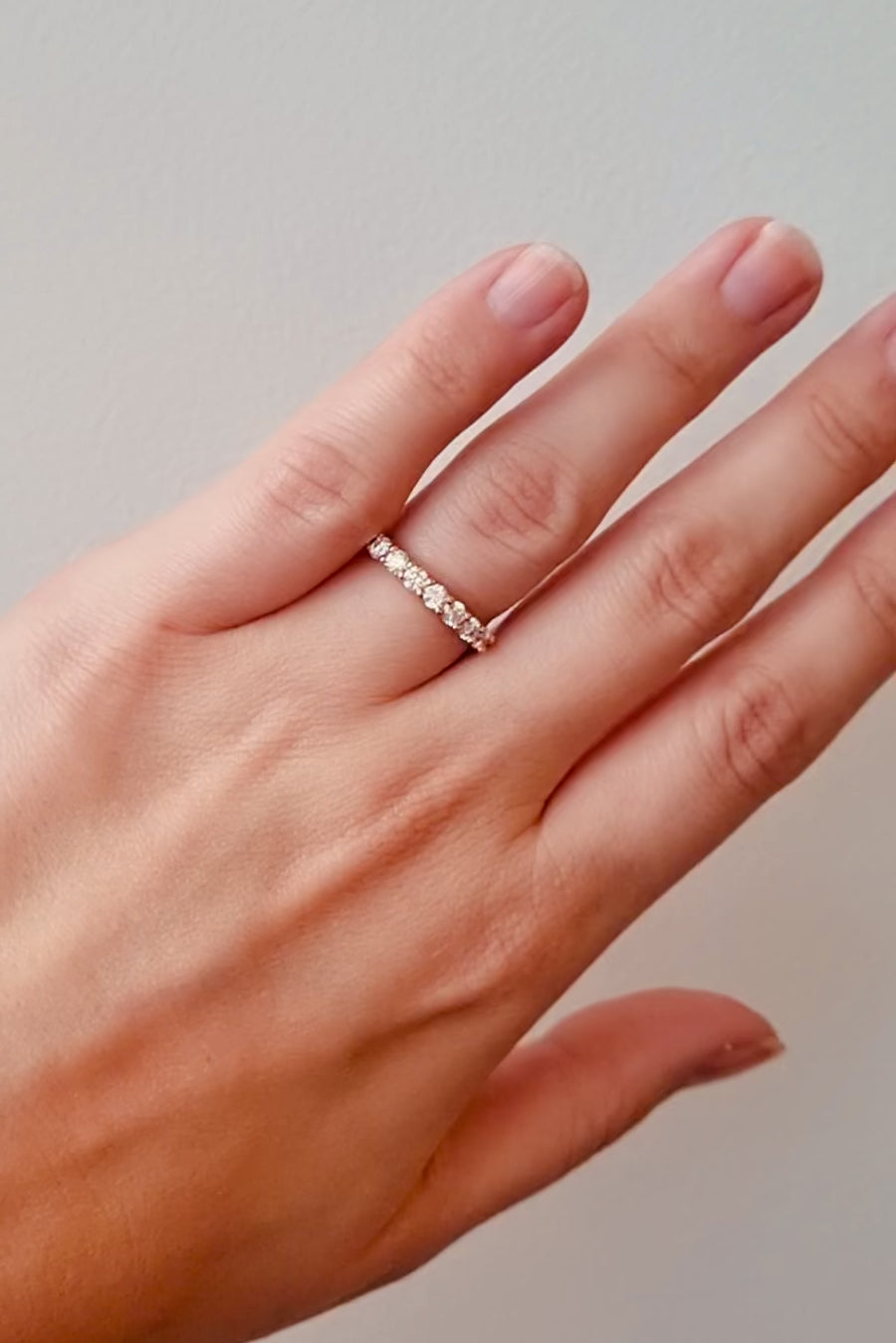 Hand wearing a rose gold diamond ring on a neutral background