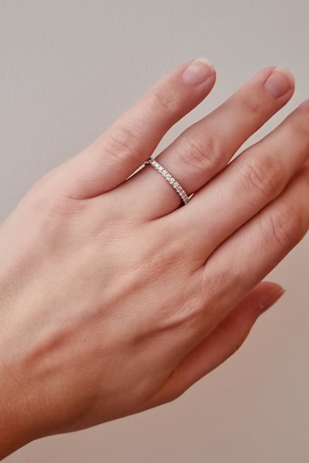 Hand wearing a white gold diamond band on a neutral background