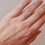 Hand wearing a white gold diamond band on a neutral background