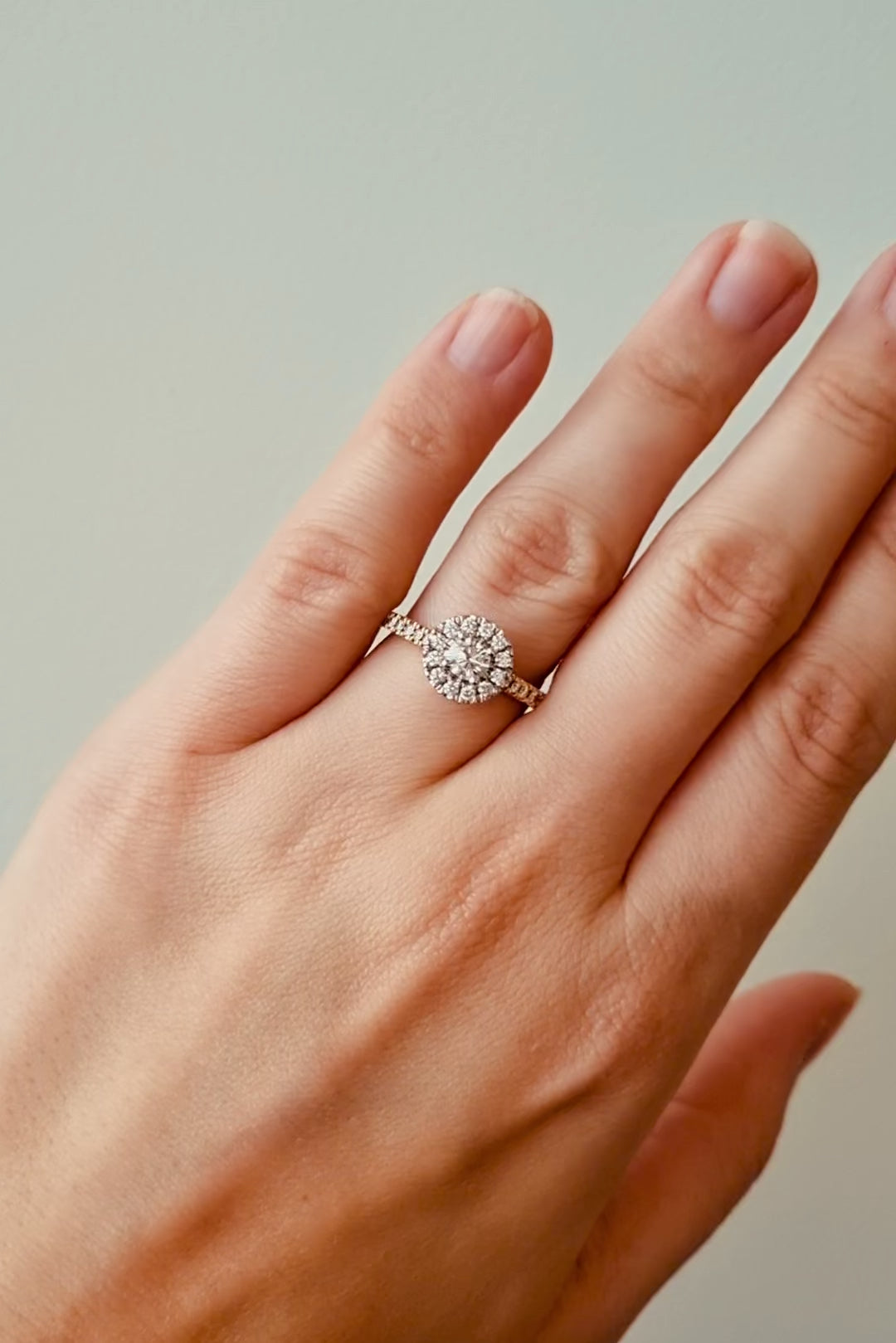 Hand wearing a diamond ring on a neutral background