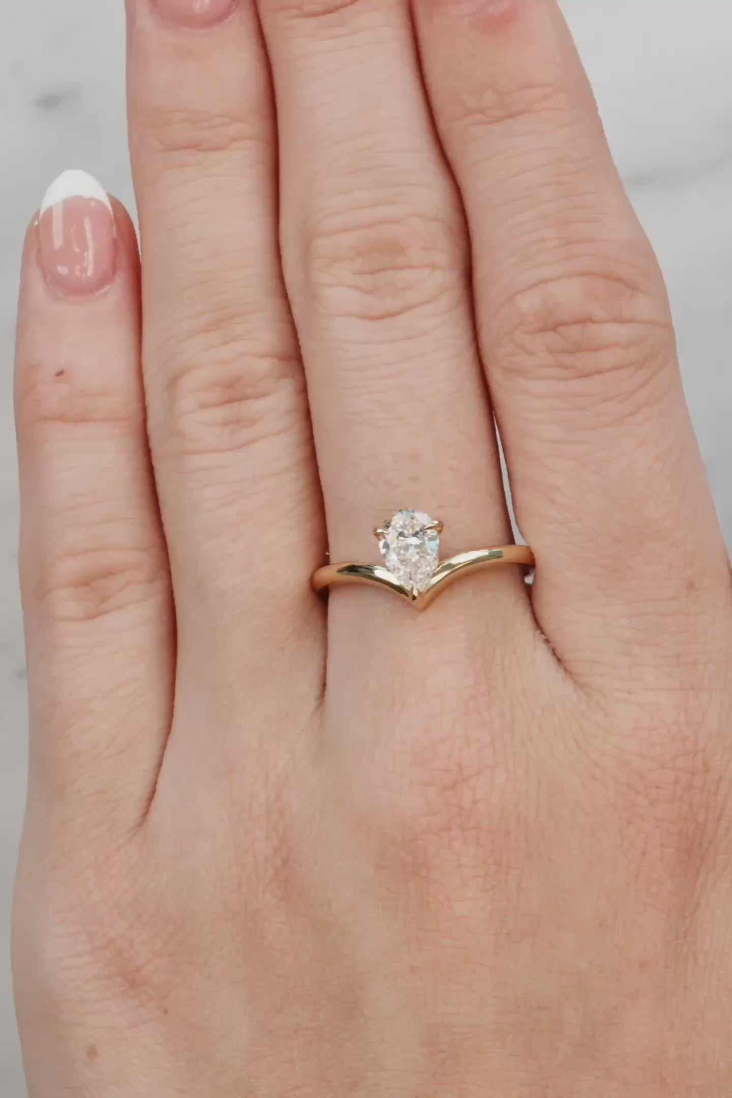 hand wearing a Gold ring with a pear-shaped diamond on a white background
