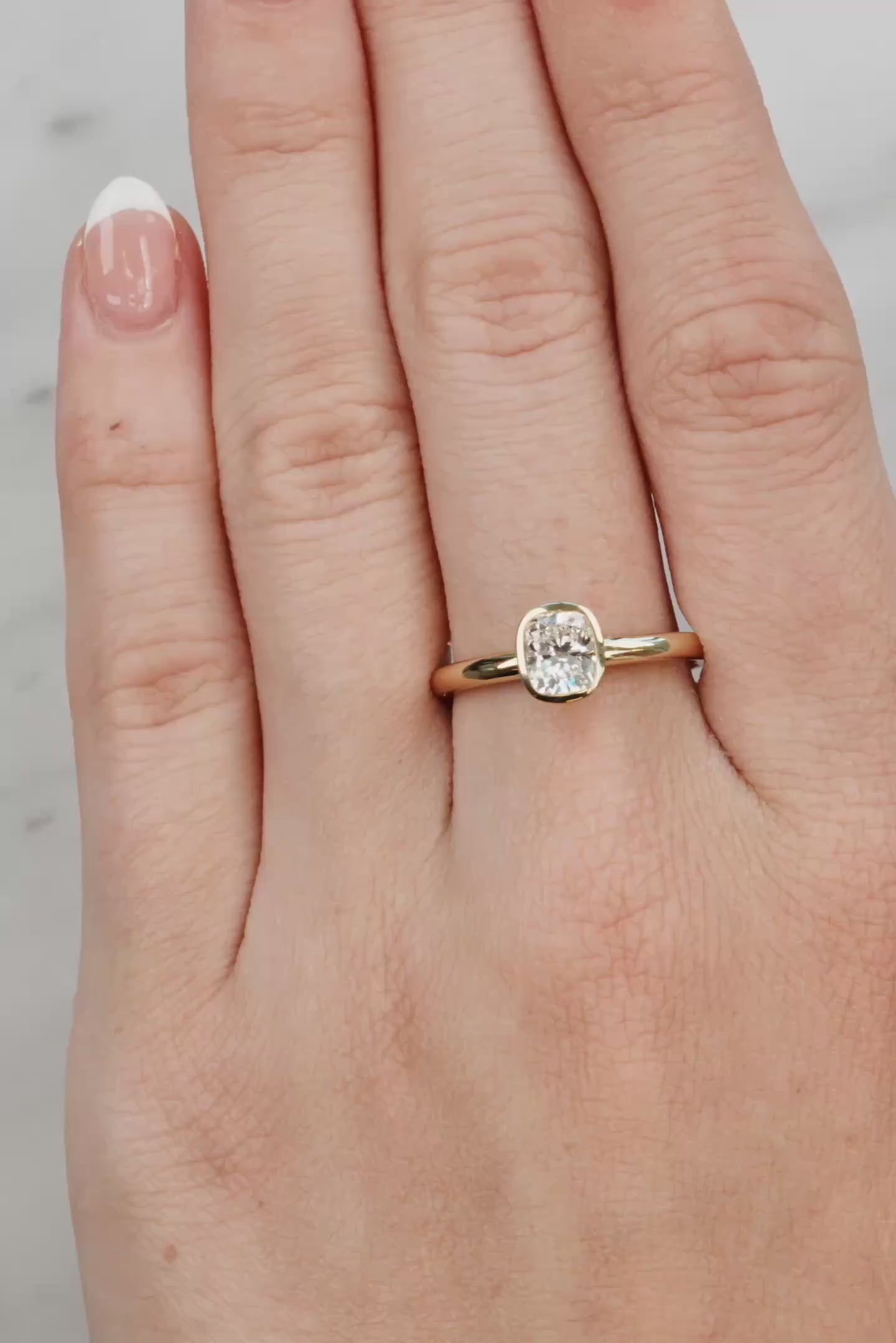 Hand wearing a gold ring with a diamond on a light gray background at LeGassick.