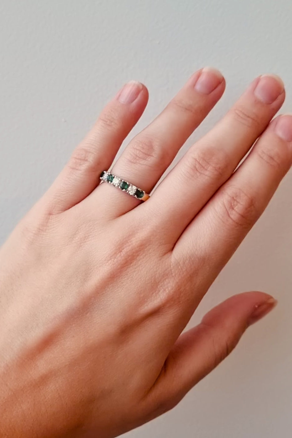 Hand wearing a gold ring with emeralds and diamonds on a white background