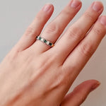 Hand wearing a gold ring with emeralds and diamonds on a white background