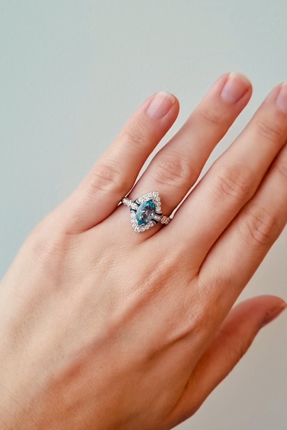 Hand wearing a ring with a blue gemstone on a neutral background at LeGassick.