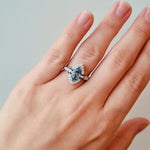 Hand wearing a ring with a blue gemstone on a neutral background at LeGassick.