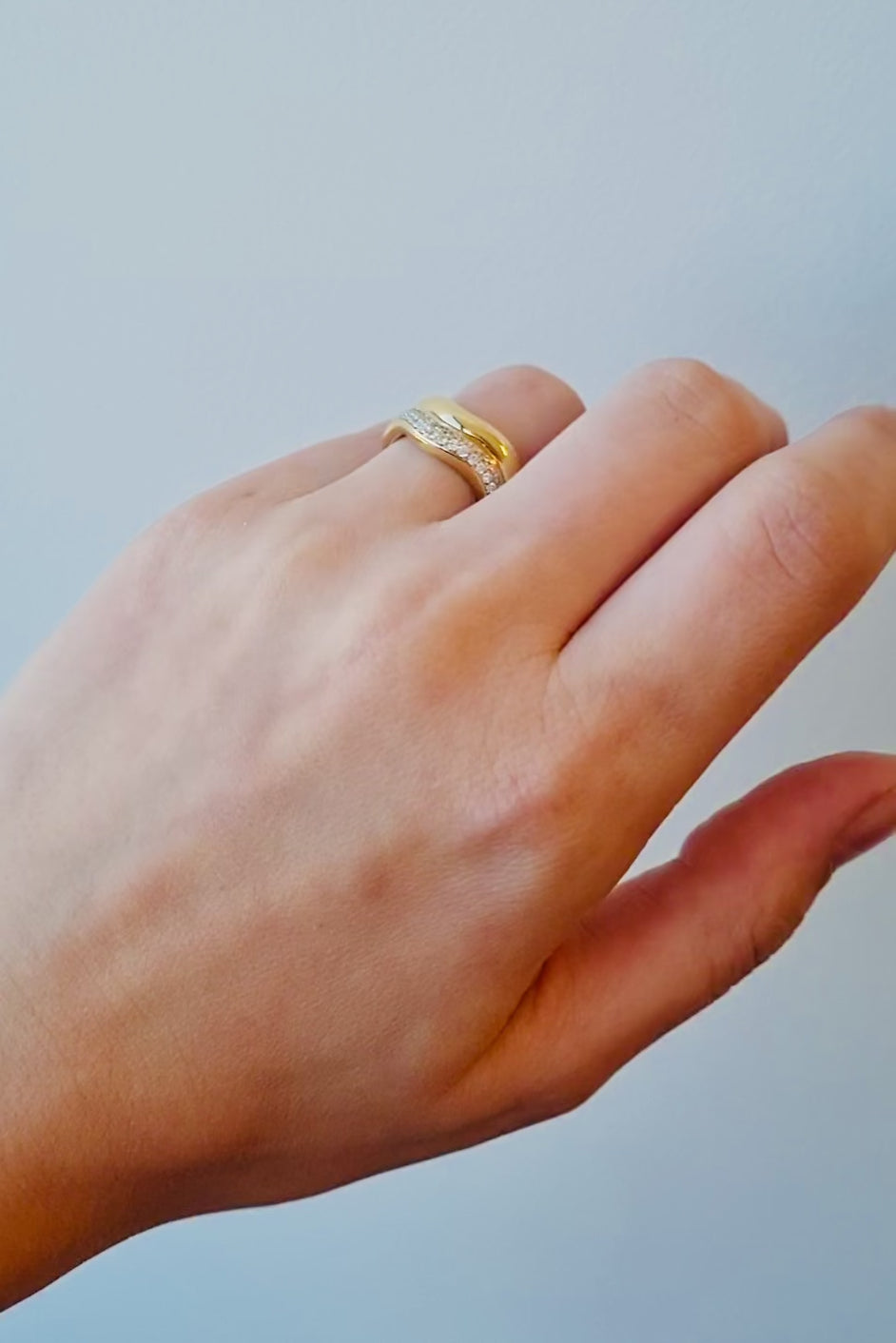 hand wearing a gold ring with diamond accents on a light background