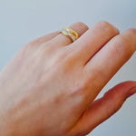 hand wearing a gold ring with diamond accents on a light background